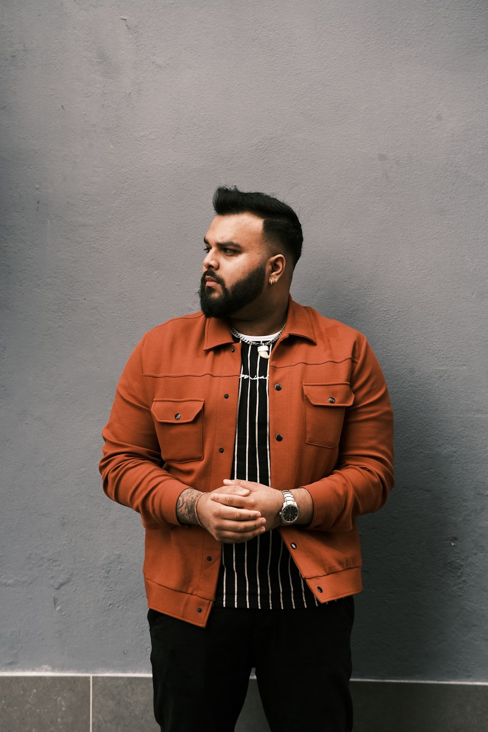 hombre con camisa de manga larga abotonada naranja de pie junto a la pared azul