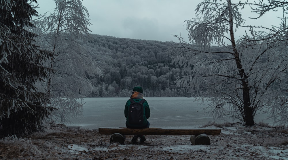 person in green jacket sitting on brown wooden bench near body of water during daytime