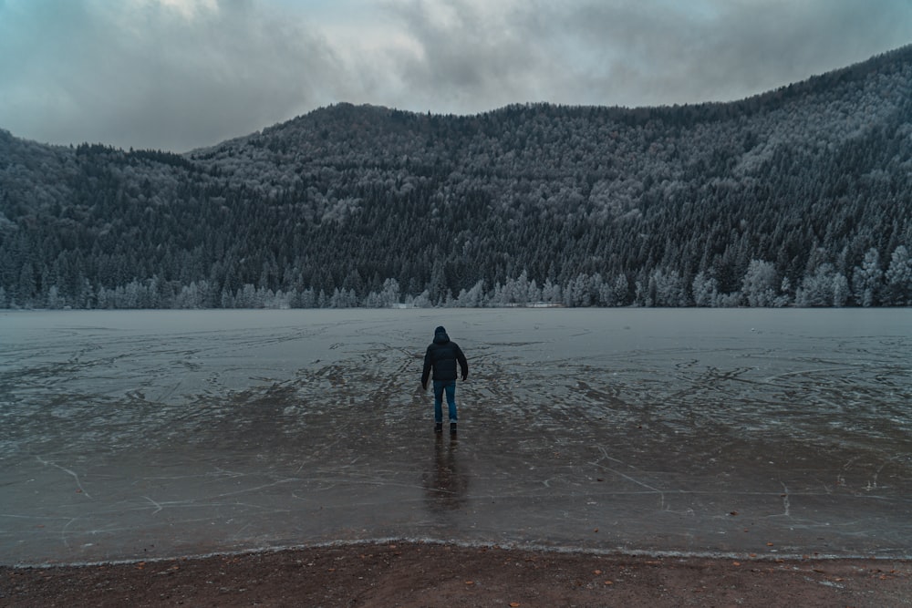 pessoa em jaqueta preta em pé no campo coberto de neve durante o dia
