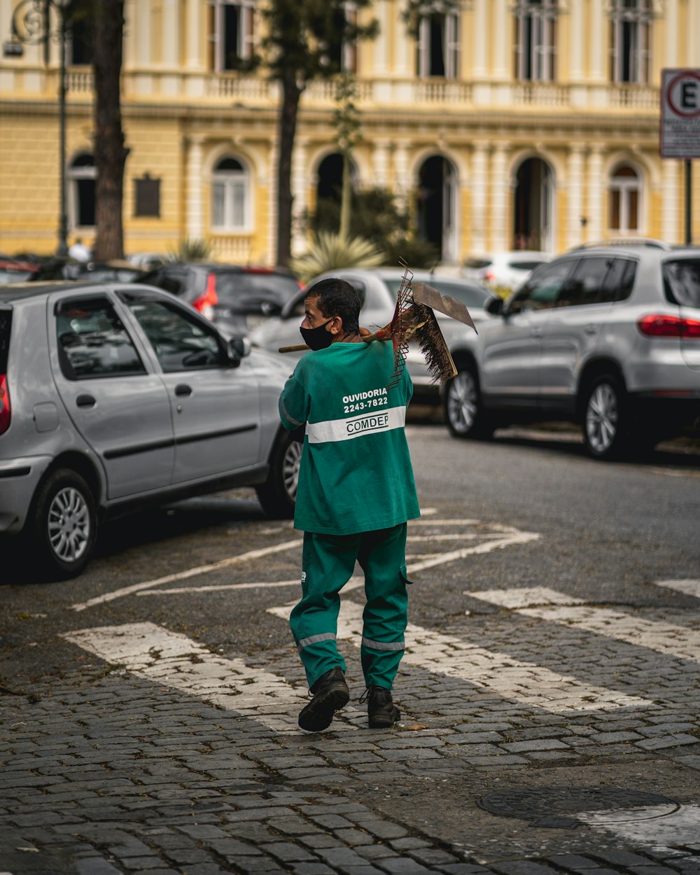 man in green jacket walking on sidewalk during daytime