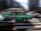 A green taxi is captured in motion against a blurred urban background, suggesting speed and dynamic city life. The taxi has a checkered stripe and a visible roof light, indicating it's a public service vehicle.