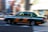 A green and white taxi is in motion, captured with motion blur effect on the background. The taxi is mid-drive on a city street, emphasizing speed and movement.