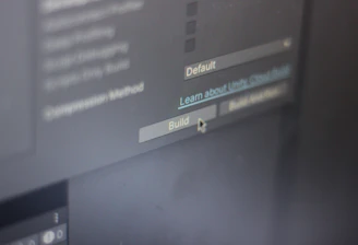 A close-up view of a computer screen displaying software development settings with options like 'Default' and 'Build' visible. A cursor hovers over the 'Build' button, suggesting interaction.