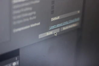 A close-up view of a computer screen displaying software development settings with options like 'Default' and 'Build' visible. A cursor hovers over the 'Build' button, suggesting interaction.