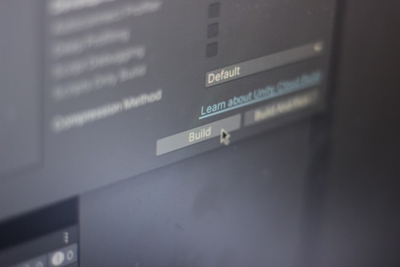 A close-up view of a computer screen displaying software development settings with options like 'Default' and 'Build' visible. A cursor hovers over the 'Build' button, suggesting interaction.