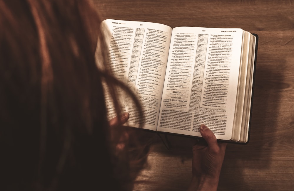 person reading book on brown wooden table