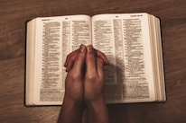 Hands joined in prayer over an open Bible with soft natural light.