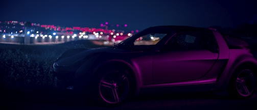A sleek luxury car photographed with neon magenta and electric green lighting effects.