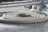 A thick white rope is coiled neatly on a ship's deck. The rope is textured and appears heavy-duty, designed for maritime use. Above the coil, there is a metal railing or support structure partially visible.