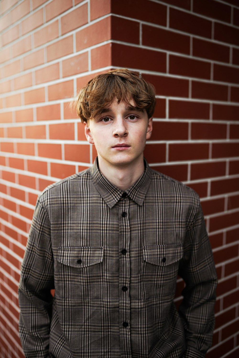 man in black and white plaid dress shirt standing beside brown brick wall