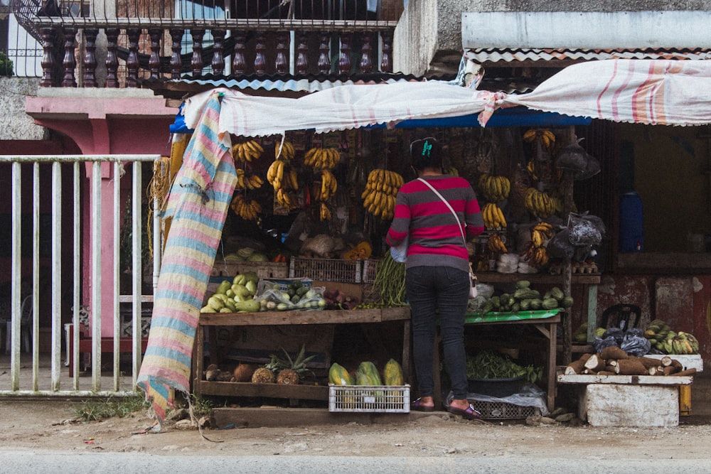 man in blue jacket and black pants standing in front of fruit stand