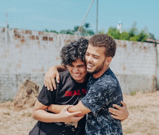 man in black crew neck t-shirt hugging woman in blue and white floral dress