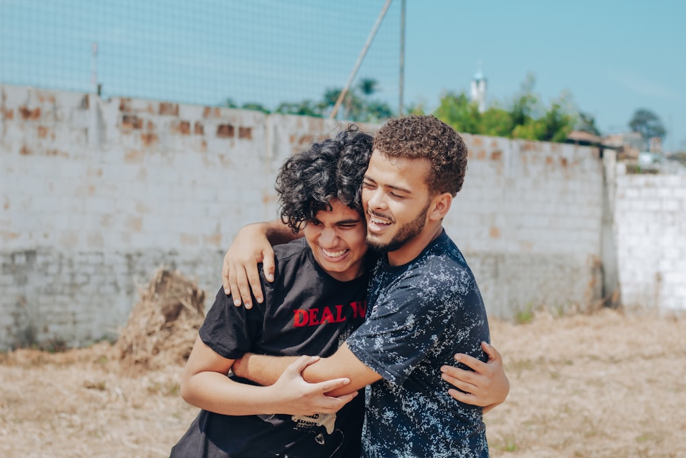 man in black crew neck t-shirt hugging woman in blue and white floral dress