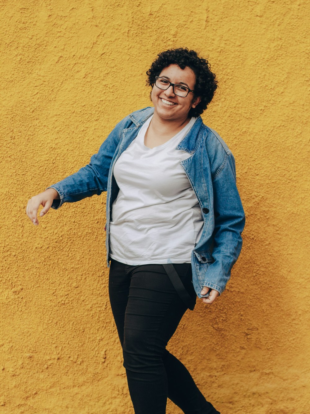 woman in blue denim jacket and black pants standing and smiling