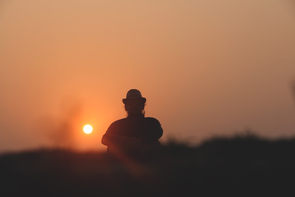 silhouette of man sitting on ground during sunset