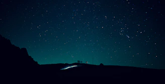 A group of people gathered around telescopes on a hilltop, gazing at a star-filled sky.