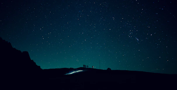 A group of people gathered around telescopes on a hilltop, gazing at a star-filled sky.
