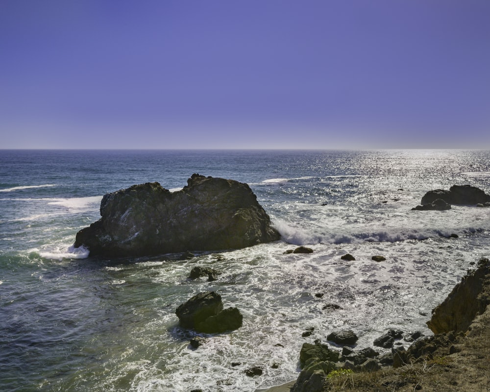 black rock formation on sea under blue sky during daytime