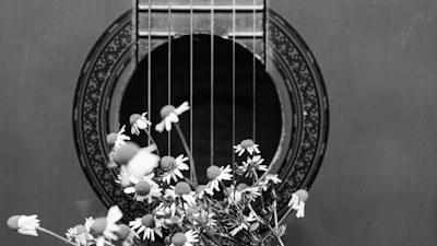 greyscale photo of white flowers on top of acoustic guitar