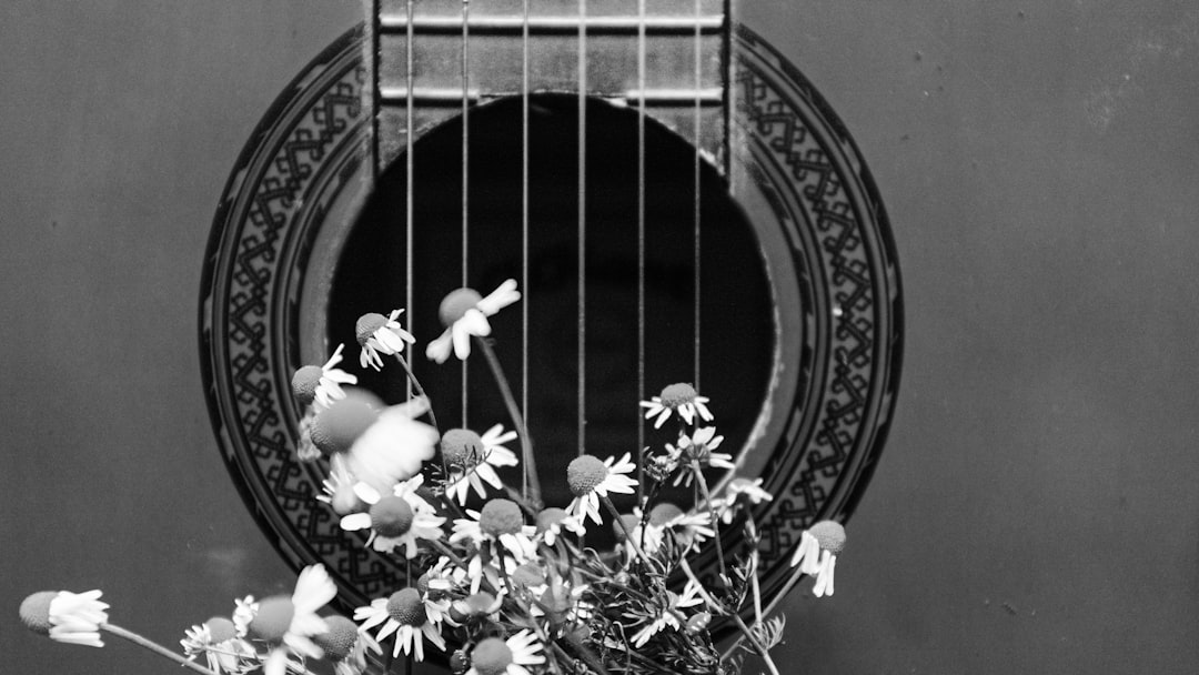 greyscale photo of white flowers on top of acoustic guitar