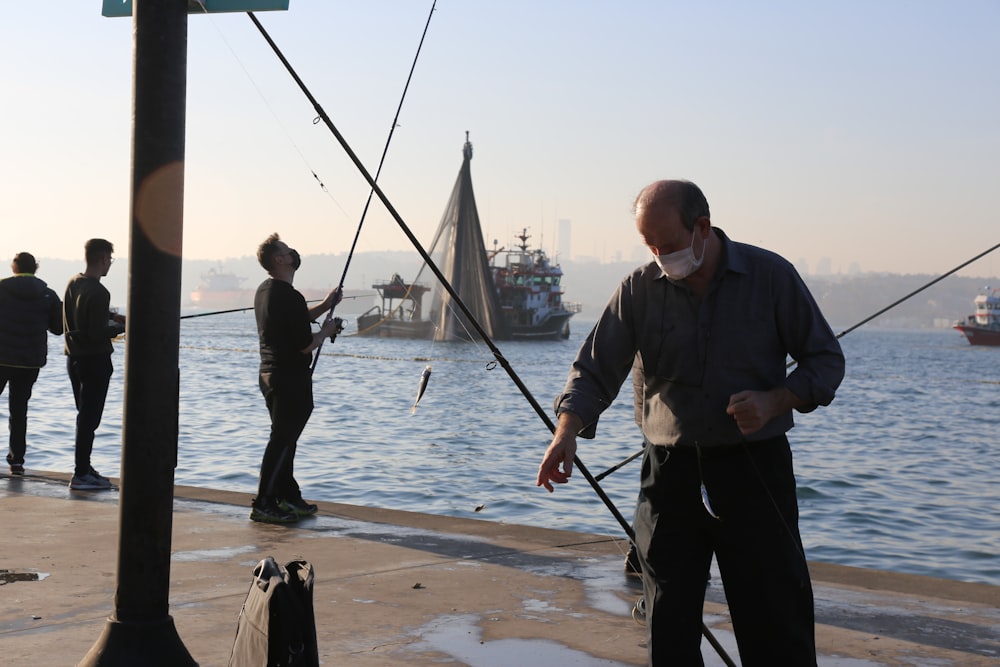 man in black jacket and black pants holding fishing rod standing on sea shore during daytime