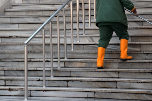 person in green jacket and brown pants walking on gray concrete stairs