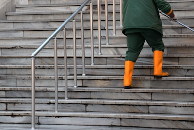 person in green jacket and brown pants walking on gray concrete stairs