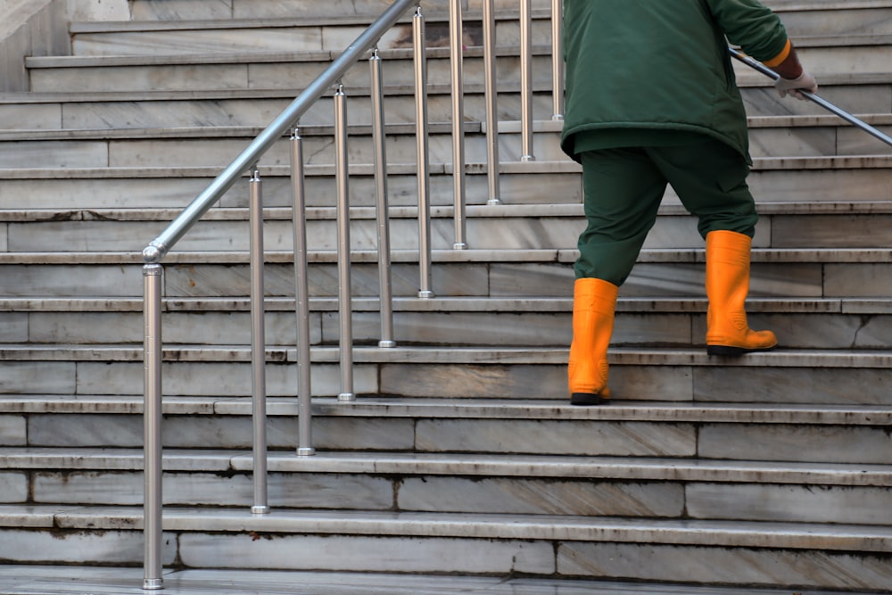 Persona con chaqueta verde y pantalones marrones caminando por escaleras de hormigón gris