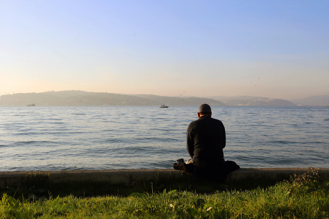 A man in a jacket sitting on a rock by the water, breathing