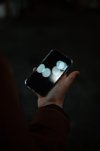 Close-up of hands holding a phone with a heart-shaped light reflection on the screen.