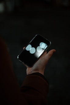 Close-up of hands holding a phone with a heart-shaped light reflection on the screen.