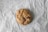 A single chocolate chip cookie rests on a crinkled piece of parchment paper. The cookie has a slightly golden-brown color with visible chunks of chocolate throughout.