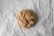 A single chocolate chip cookie rests on a crinkled piece of parchment paper. The cookie has a slightly golden-brown color with visible chunks of chocolate throughout.