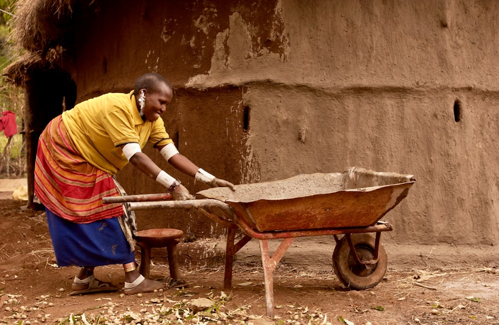 man in yellow polo shirt and blue denim jeans holding brown wheelbarrow