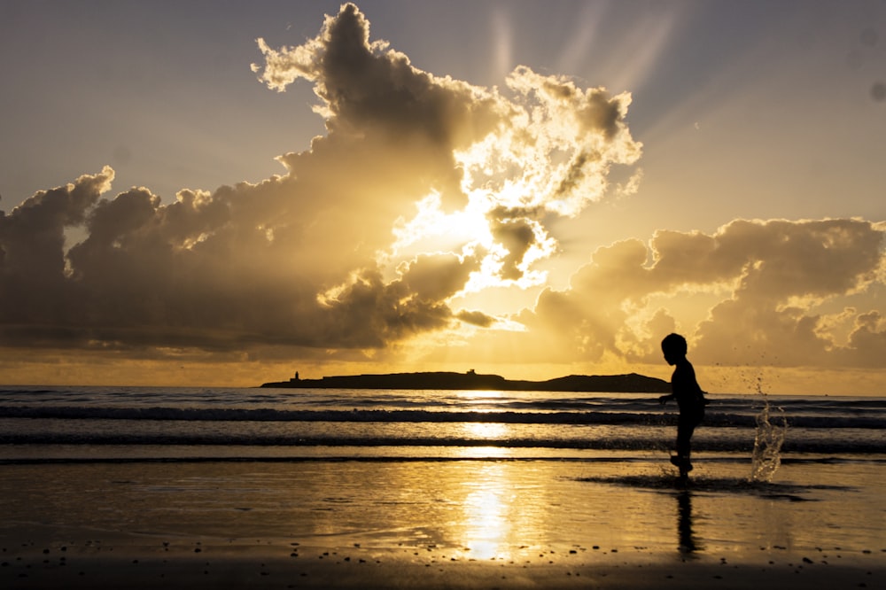 silhueta do homem que caminha na praia durante o pôr do sol