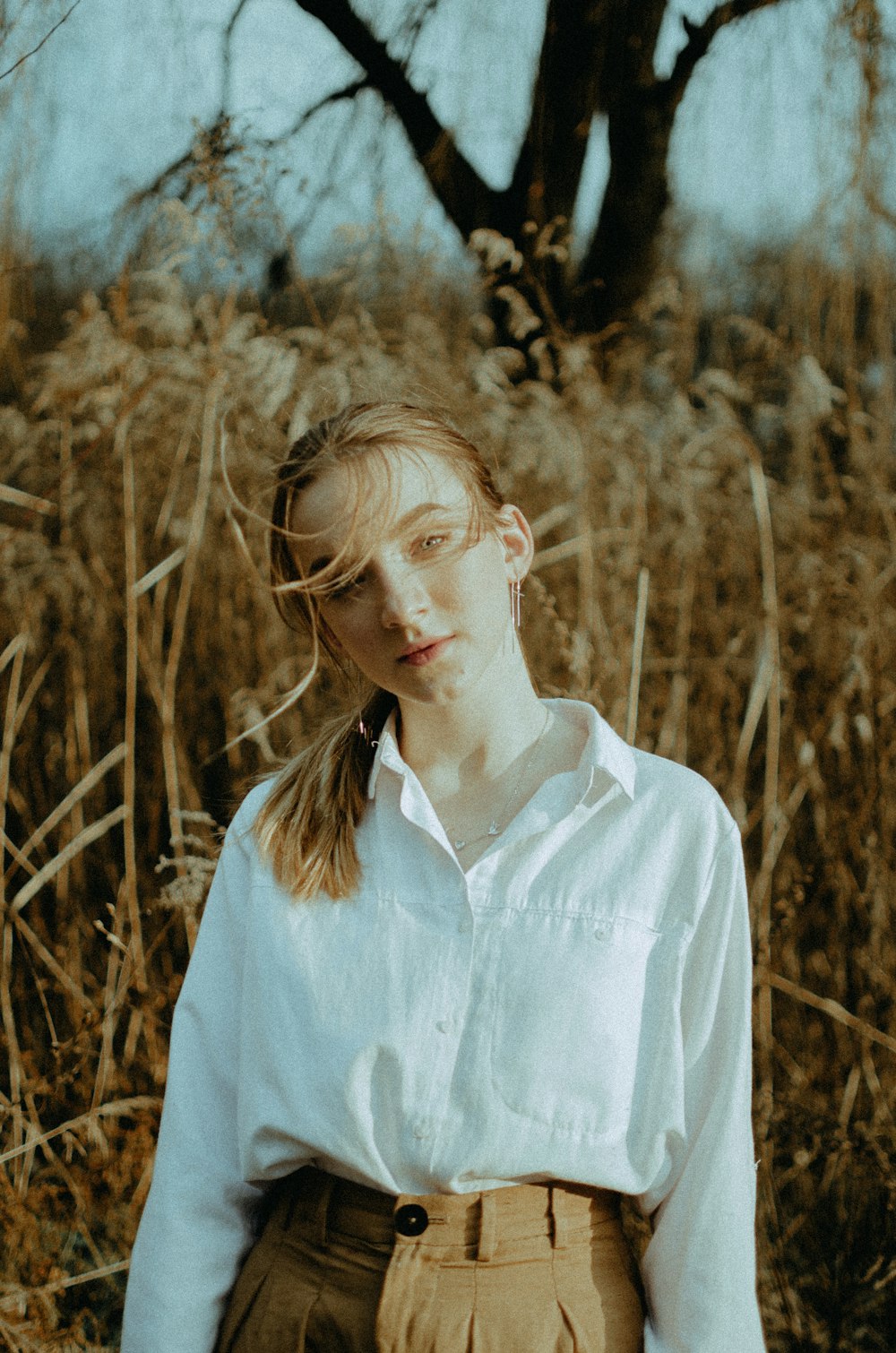 woman in white dress shirt standing on brown grass field during daytime