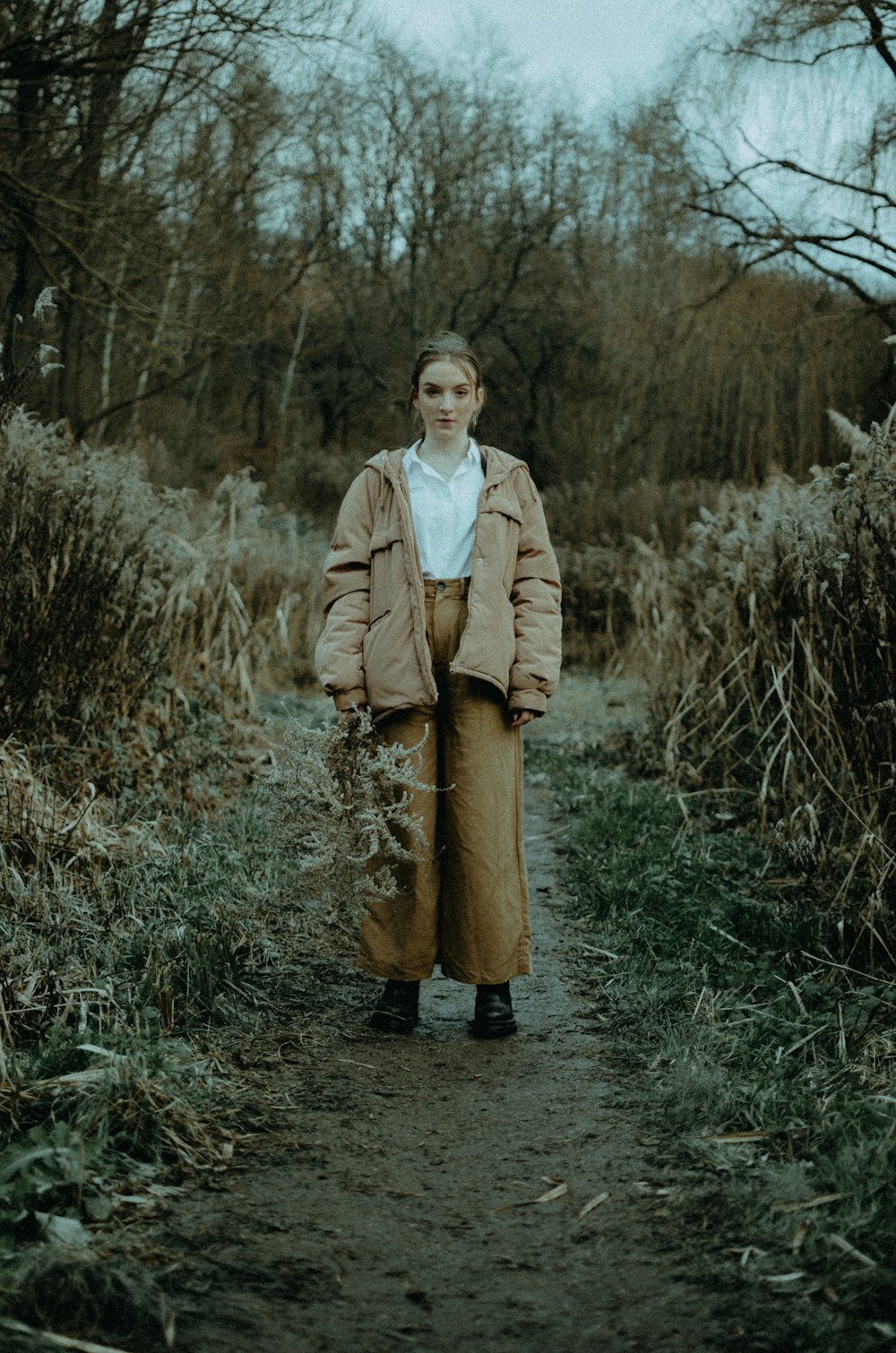 woman in brown coat standing on dried grass