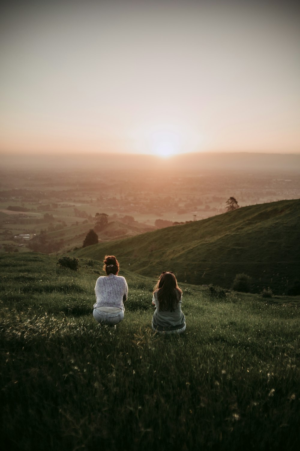 woman in white shirt sitting on green grass field during sunset