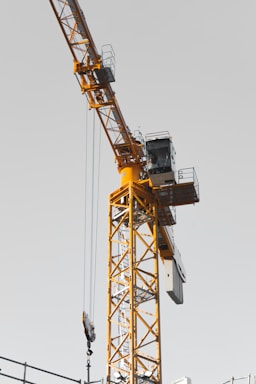 A rugged yellow crane towering over a busy construction site under a clear sky.