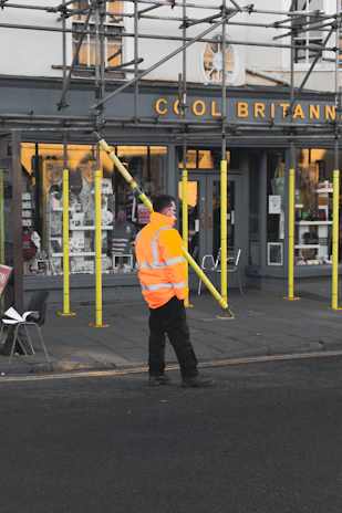 man in yellow jacket and black pants walking on sidewalk during daytime