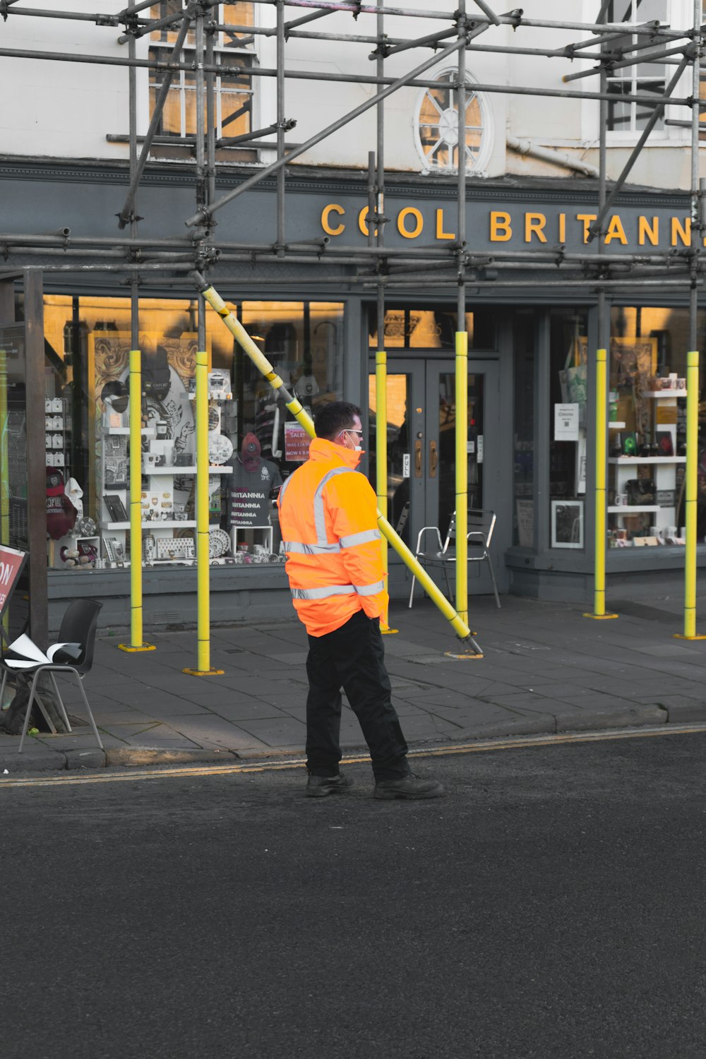 man in yellow jacket and black pants walking on sidewalk during daytime