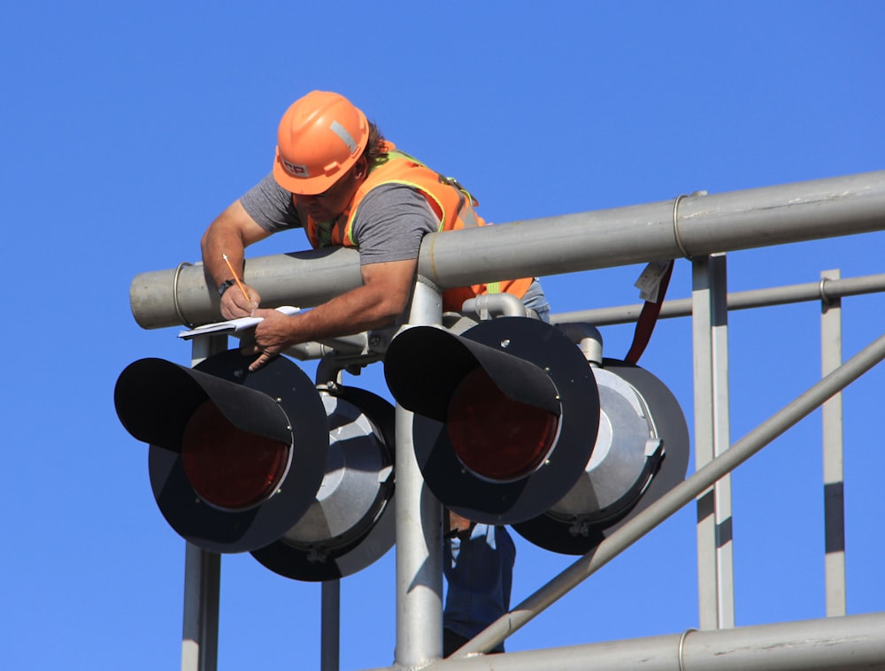 man in orange helmet climbing on white metal bar during daytime