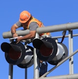 man in orange helmet climbing on white metal bar during daytime