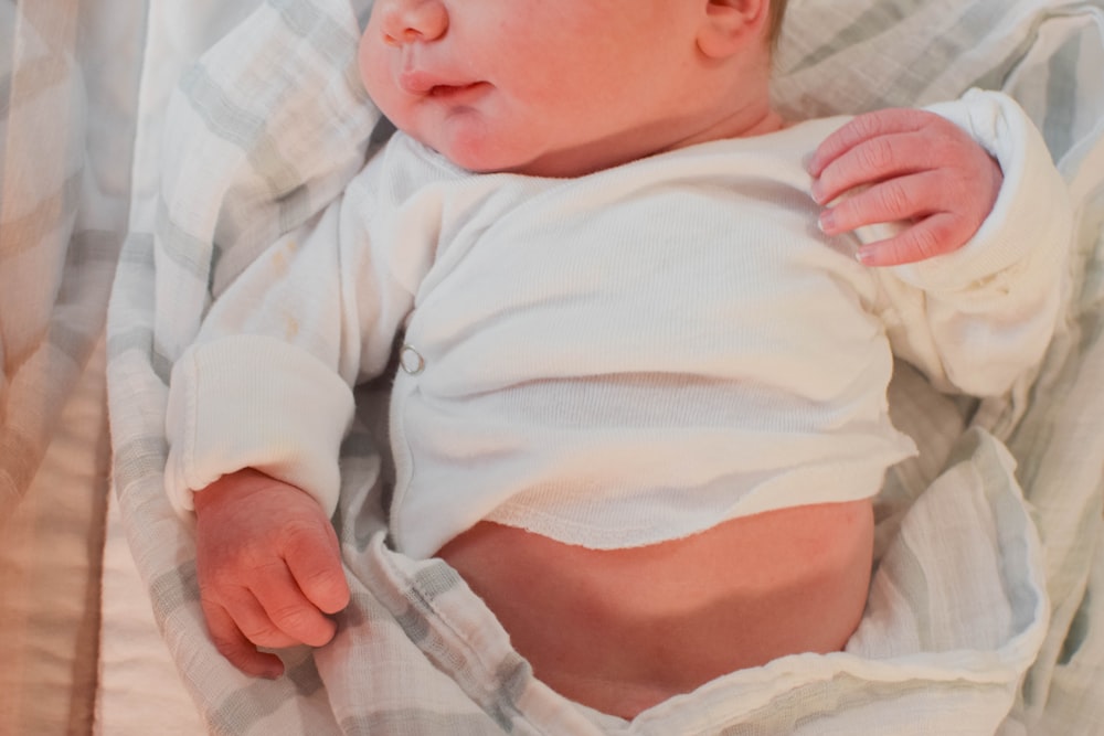 baby in white onesie lying on bed