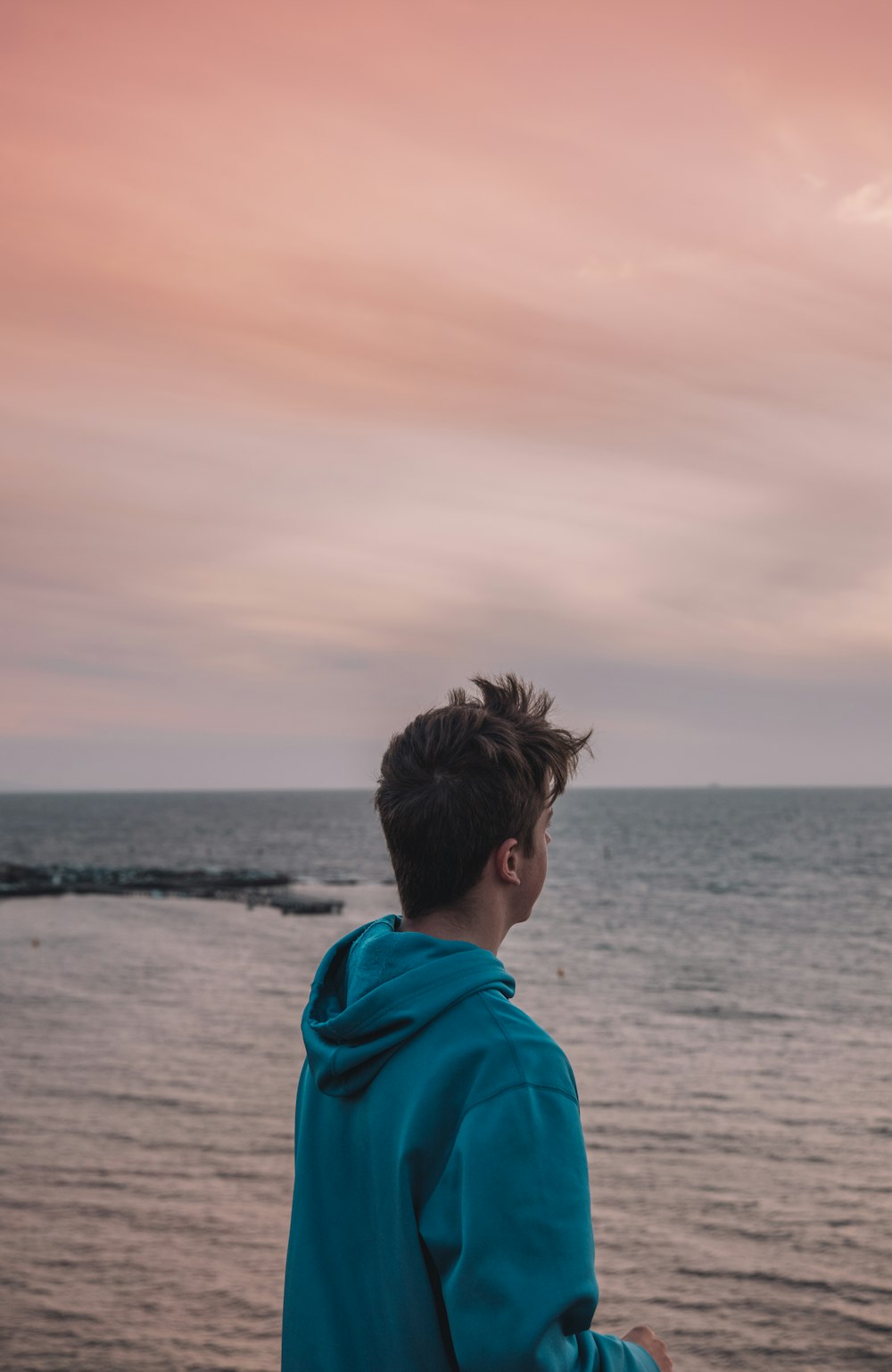 man in blue hoodie standing on beach during daytime