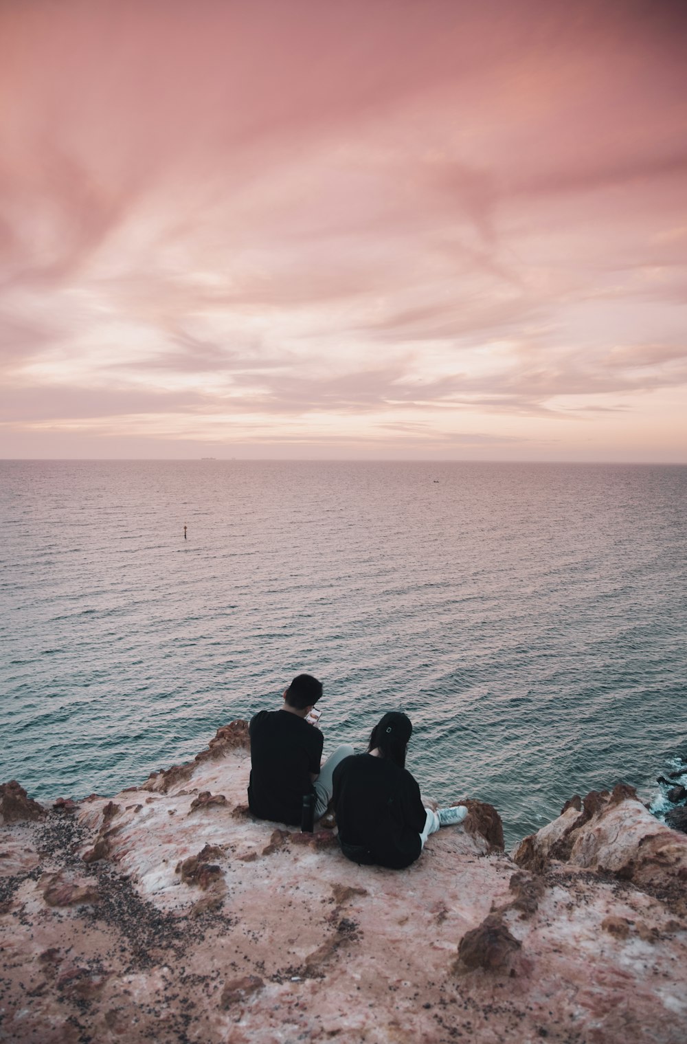 2 men sitting on brown rock near body of water during daytime