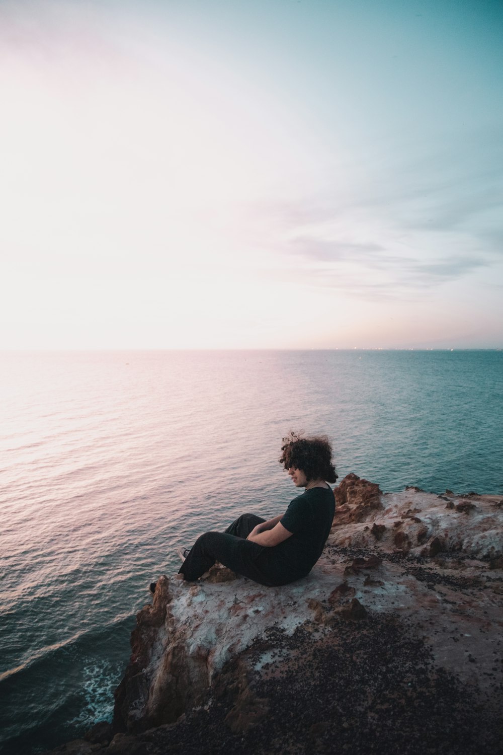 Mujer con camisa negra sentada en la roca junto al mar durante el día