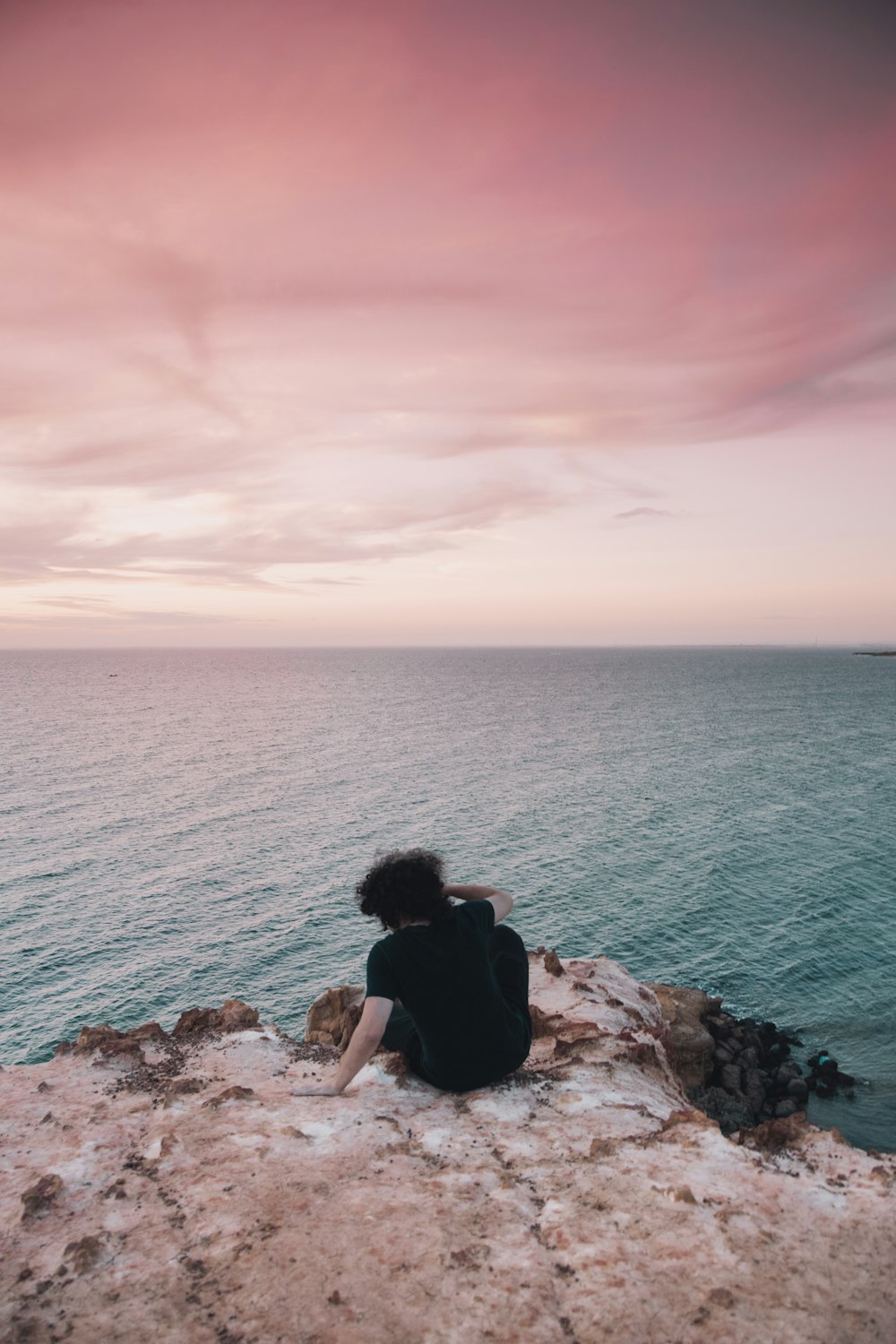 woman in black tank top sitting on brown rock formation near body of water during daytime