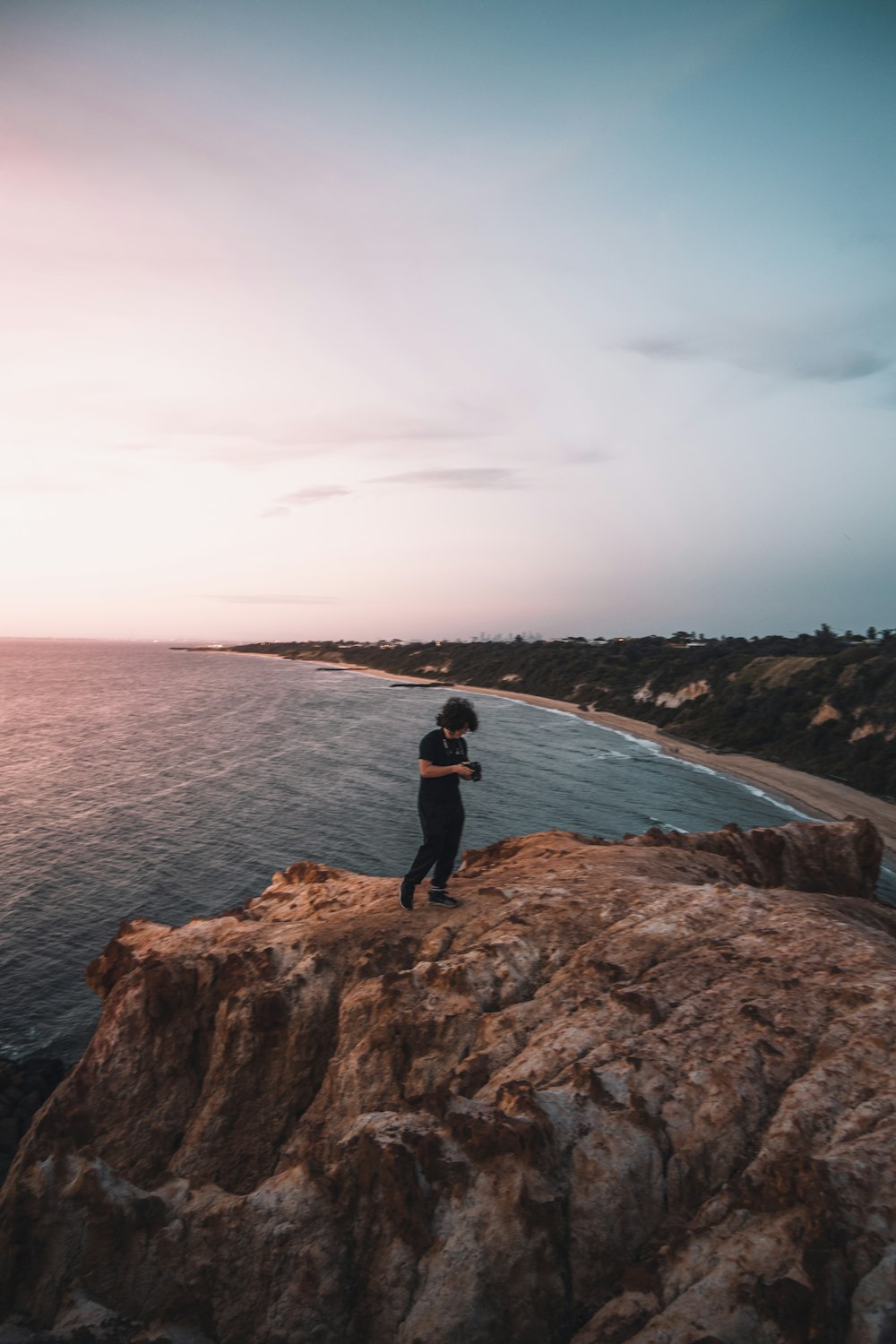 man in black jacket standing on brown rock formation near body of water during daytime