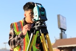 man in gray and orange jacket holding green and black dslr camera during daytime